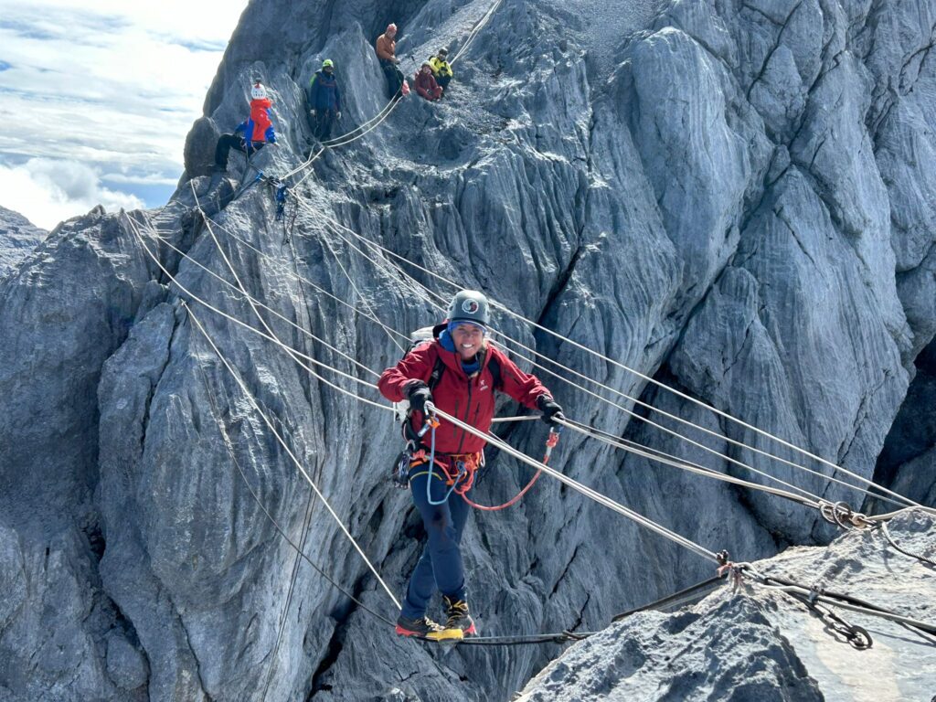Climber crossing a rope bridge on the extreme trail of Carstensz Pyramid, Papua, with steep limestone cliffs in the background