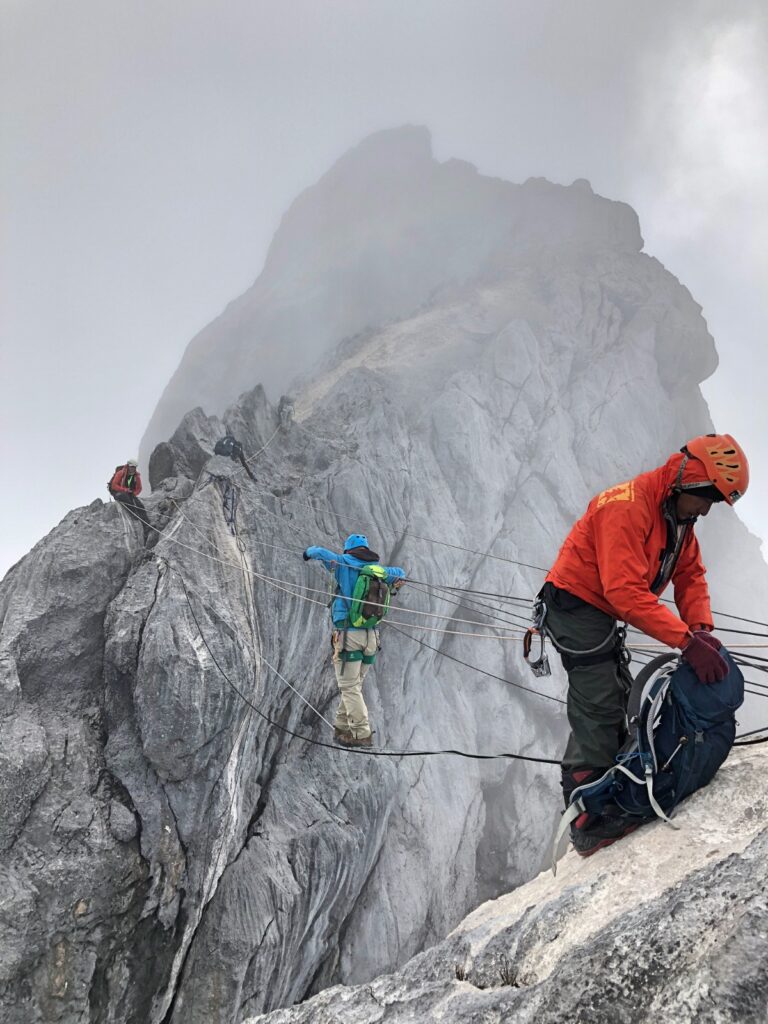 Climber crossing a rope bridge fully equipped on the extreme route of Carstensz Pyramid, shrouded in thick fog