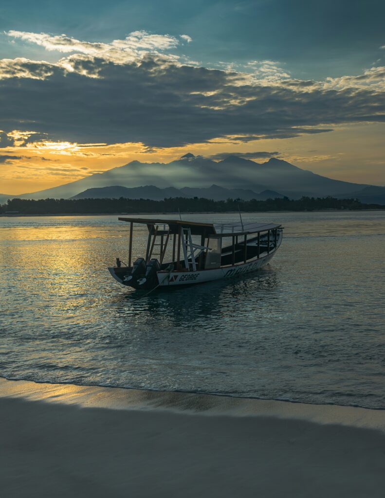 Pantai di Gili Trawangan dengan pasir putih, air laut jernih, dan perahu kecil terapung di kejauhan.