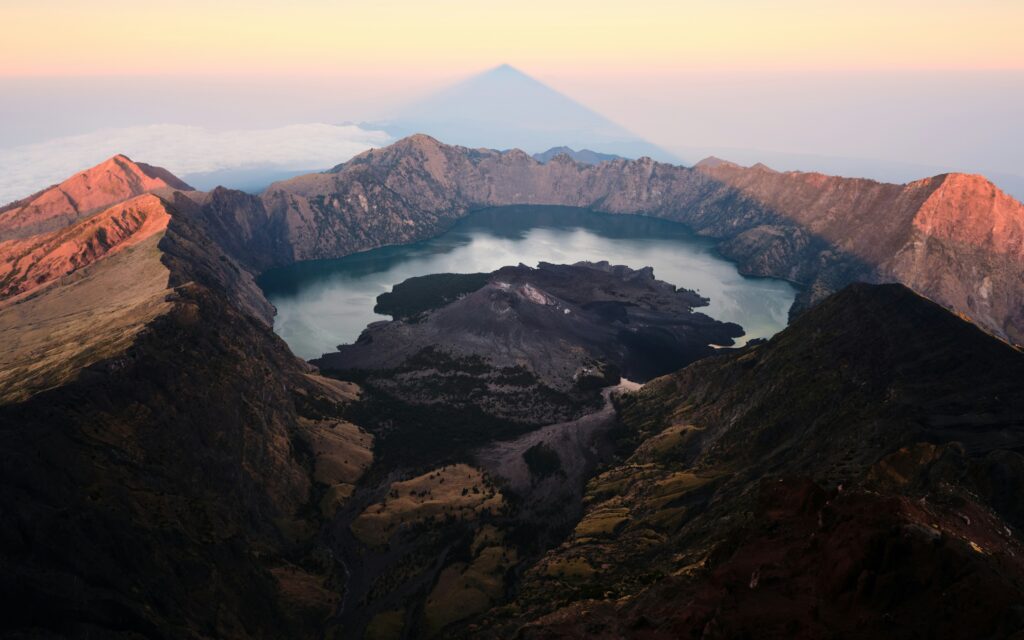 Puncak Gunung Rinjani,Nusa Tenggara Barat(NTB) dengan Danau Segara Anak terlihat di bawahnya, diselimuti kabut pagi dan langit biru.