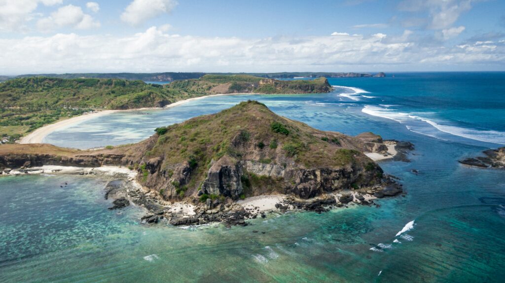 Pemandangan Pantai Kuta Mandalika di Lombok dengan pasir putih halus dan laut biru jernih di bawah langit cerah.