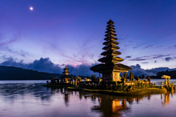Pura Ulun Danu Beratan di Bedugul Bali saat matahari terbit dengan latar langit ungu dan pantulan danau yang tenang.