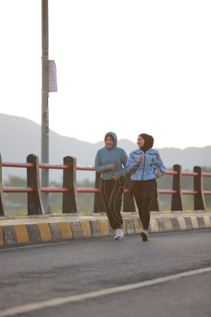 Dua wanita berlari santai di jalanan dengan latar pegunungan saat pagi hari, mencerminkan tren running sebagai gaya hidup sehat.